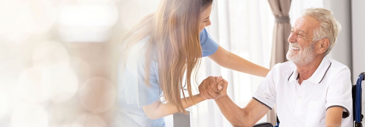 pflegehelfer ausbildung zeigt junge helferin beim betreuen eines seniors im rollstuhl am fenster
