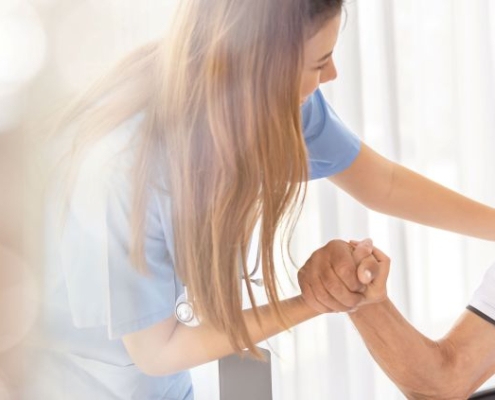 pflegehelfer ausbildung zeigt junge helferin beim betreuen eines seniors im rollstuhl am fenster