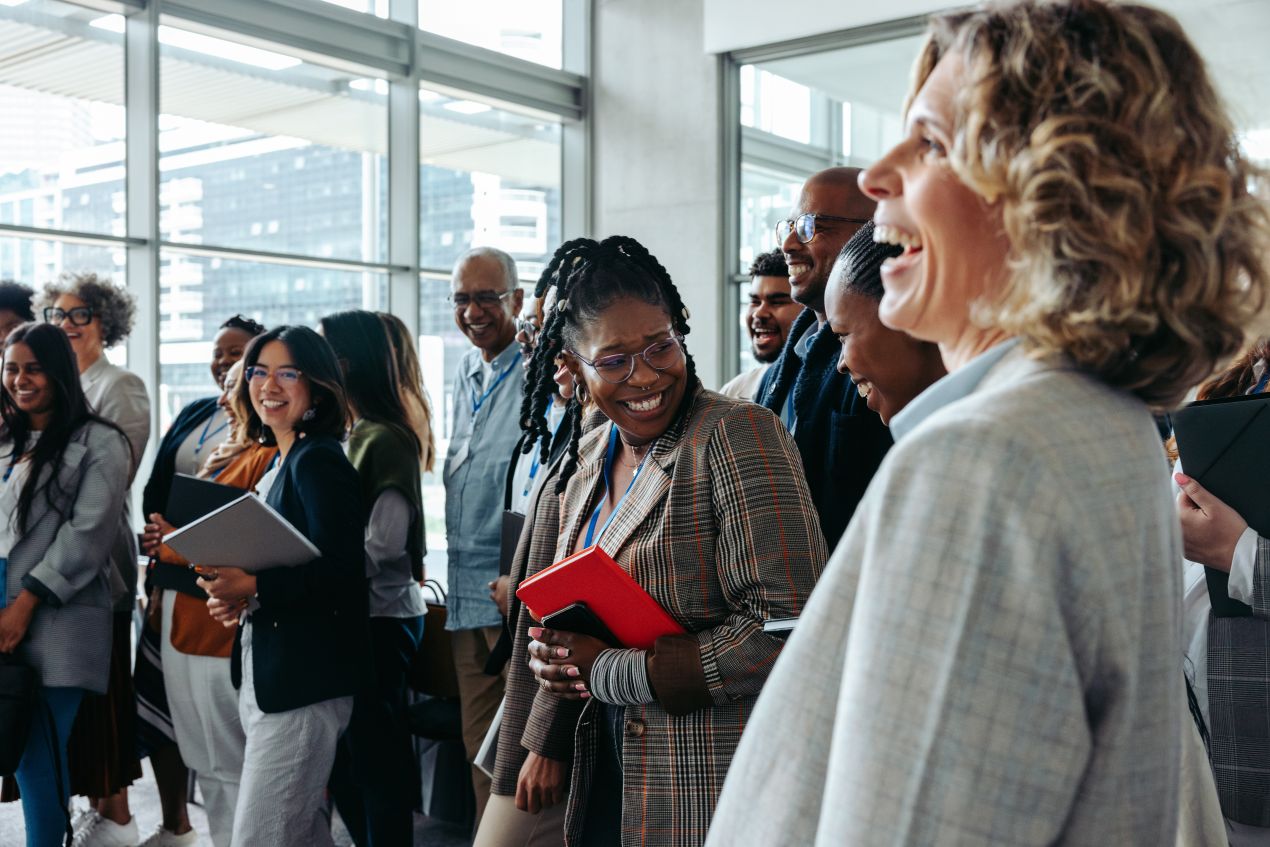 Lächelnde Fachleute bei einem Networking-Event, lebhafte Gespräche und positive Atmosphäre, Eventmoderator im Hintergrund sorgt für Struktur