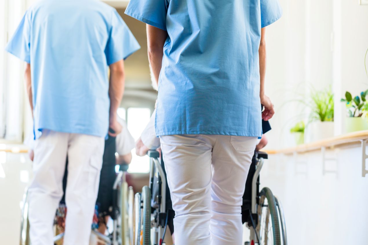 pflegehelfer ausbildung mit praxisanteil zeigt helfer beim schieben von rollstuehlen im pflegeheim