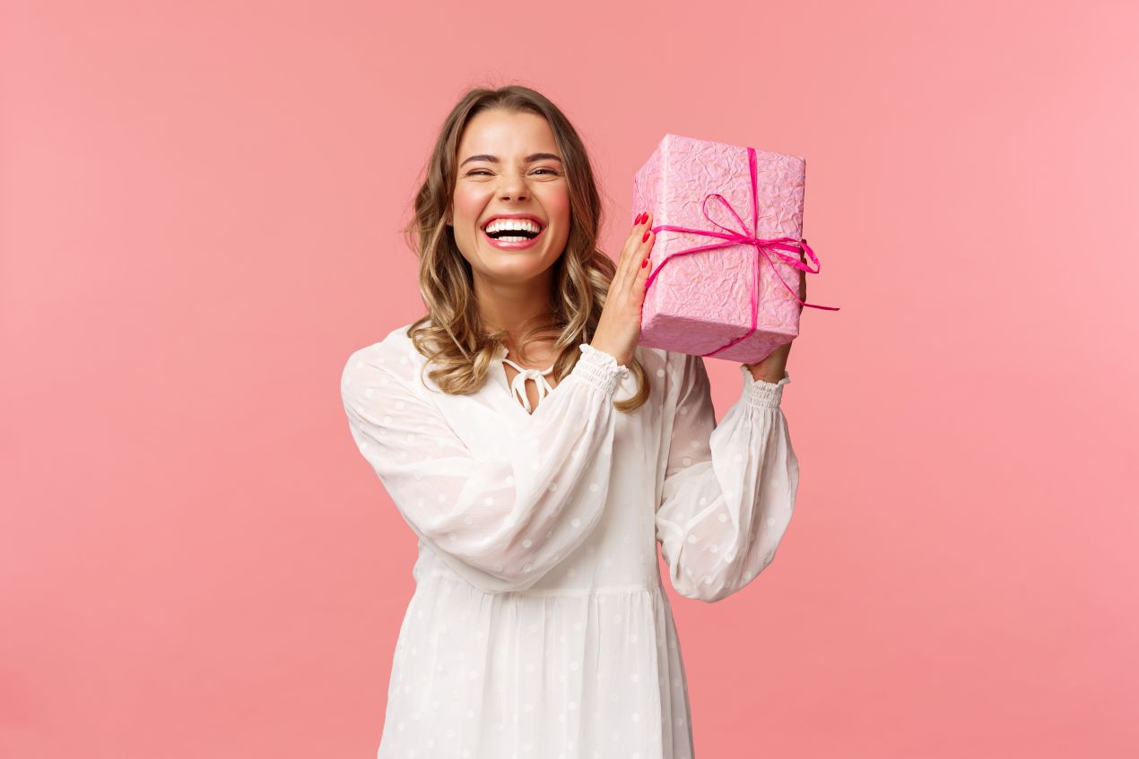 Junge Frau freut sich ueber ein rosa verpacktes Geschenk – praesentkorb als kreative Geschenkidee mit emotionaler Wirkung
