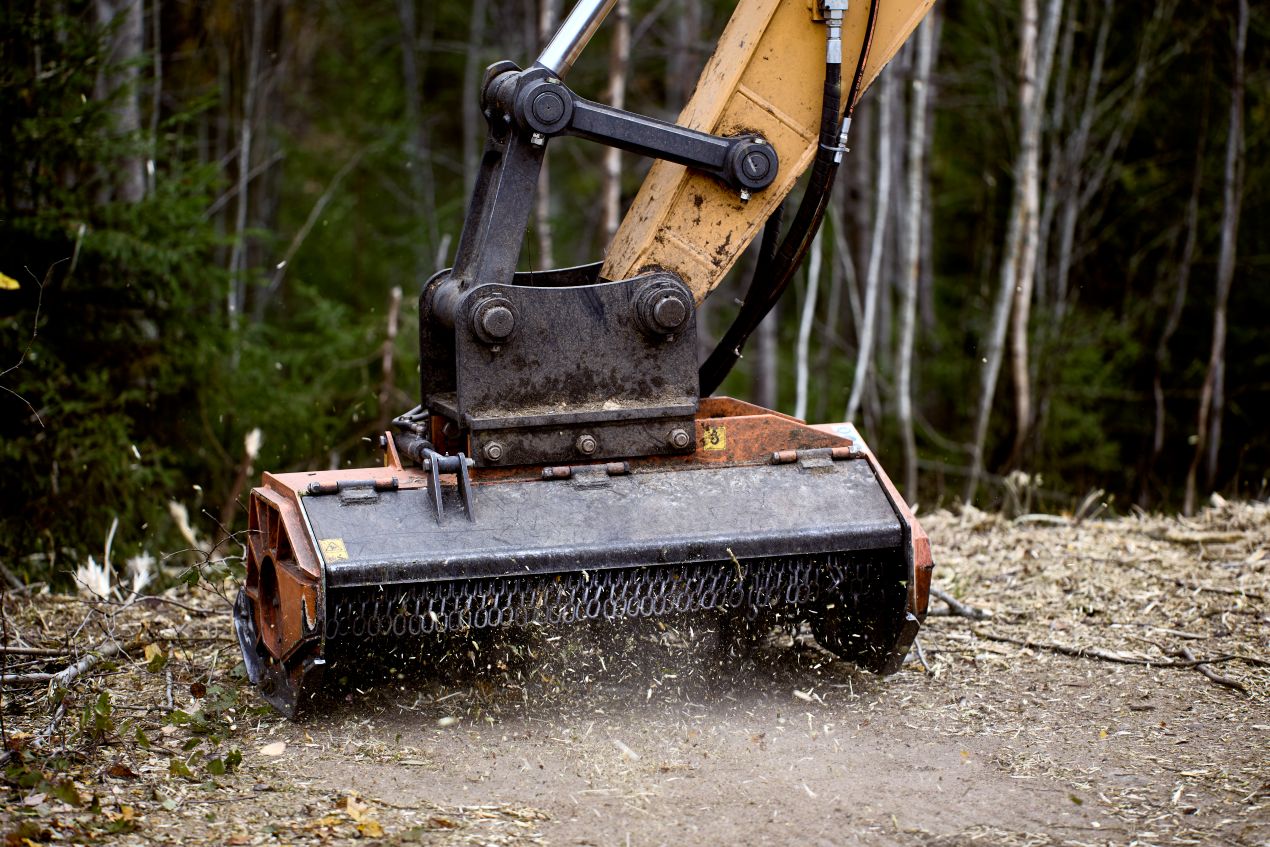 Forst-Mulchgeraet als Flaechenhaecksler an einem Bagger im Wald im Einsatz auf schwierigem Untergrund