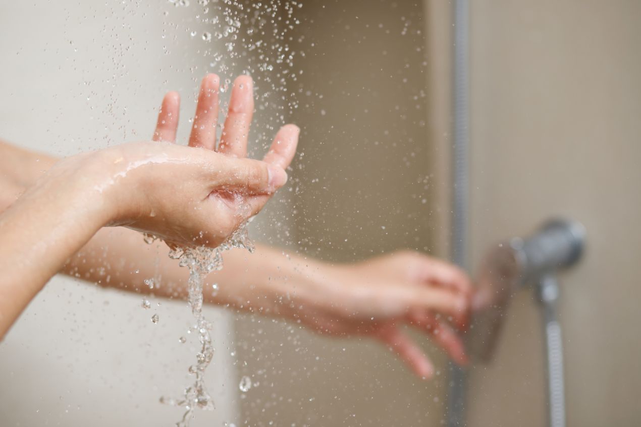Haende unter laufendem Wasser vor glatter Duschrueckwand in moderner Dusche