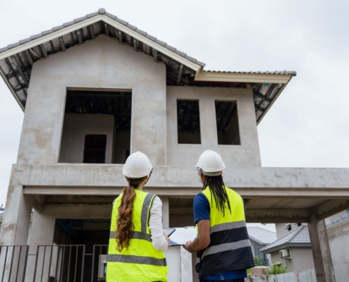 Zwei Fachkräfte mit Schutzhelmen vor Rohbau