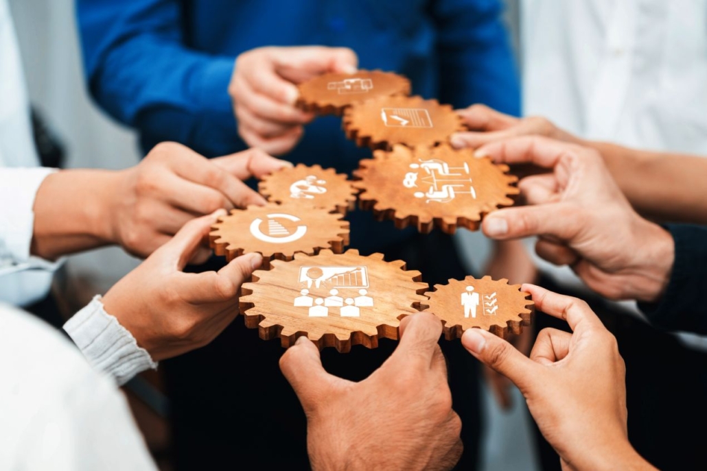 Mehrere Hände greifen ineinander greifende Zahnräder mit Symbolen – Symbolbild für Teamarbeit und strategische Planung bei Multimode-Netzwerken