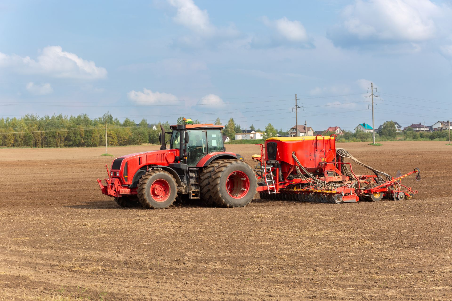 Roter Traktor mit großem Anbaugerät auf Ackerfläche, Beispiel für den Einsatz eines hydraulischen Oberlenkers